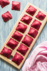 Preparing homemade pink ravioli (tortellini) with goat cheese on blue wooden table. Selective focus
