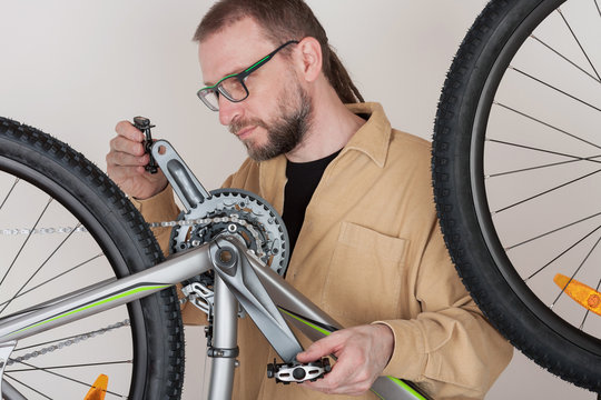 Bearded man screws the pedals on the mtb bicycle.