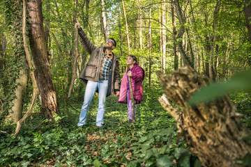 Naklejka na ściany i meble Young father is hiking with his daughter in the woods and pointing at something to her