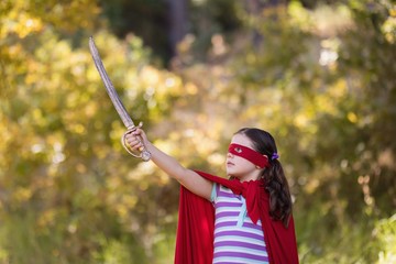 Fototapeta premium Little girl holding sword while wearing superhero costume