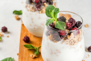 Dietary vegan healthy breakfast. Yogurt and granola with fresh blackberry oranges and mint in a glass. On a white table, on a cutting board. Copy space close view