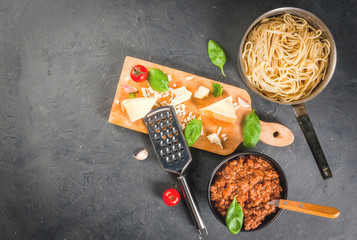 Ingredients of Italian cuisine. Products for the preparation of pasta bolognese, the cooking process. Welded spaghetti in pan, bolognese sauce, basil, garlic, tomato, parmesan Top view copy space
