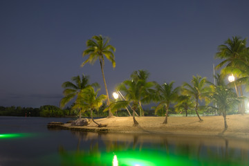 Sandy beach at Camana Bay in the Caribbean illuminated by hanging lanterns from palm trees, Grand...