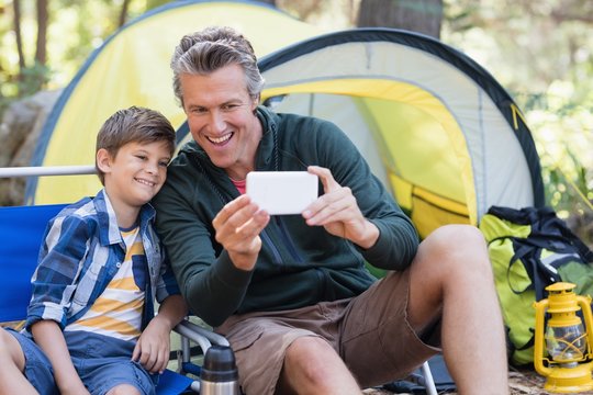 Father and son taking selfie by tent in forest