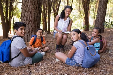 Portrait of happy teacher and students sitting in forest