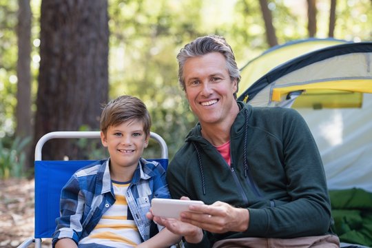 Smiling father and son using mobile phone by tent in forest