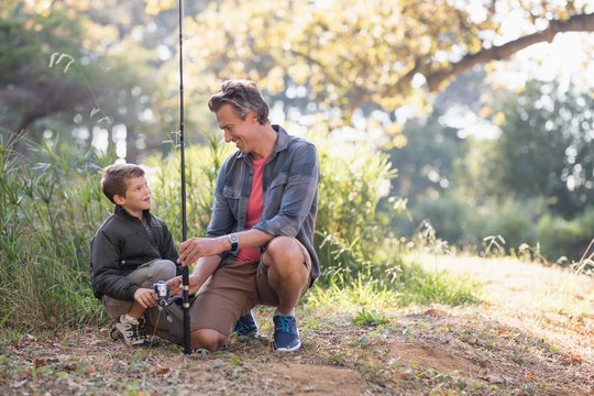 Father and son looking at each other while holding fishing rod 