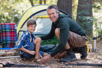 Cheerful father and son kneeling by tent in forest