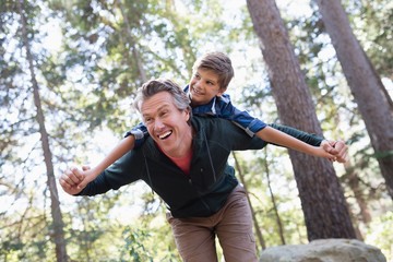 Cheerful father piggybacking son in forest