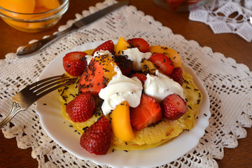 Fresh homemade pancakes with strawberries, apricots,cream and chocolate on a white plate.