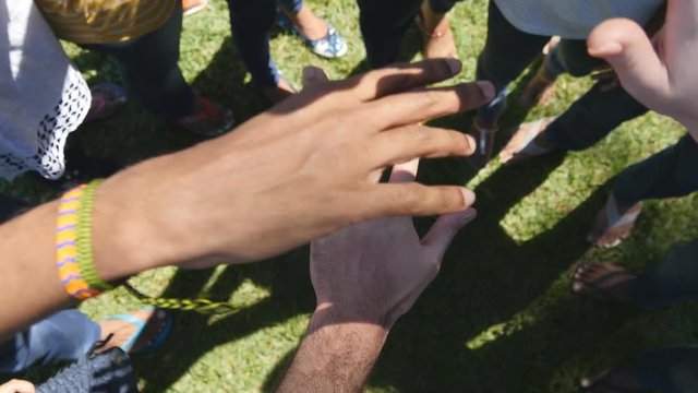 Arm of all races and colors stacked together one by one in unity and teamwork and then raised. Many multiracial hands getting together in the center of a circle and then cheer. Close up outdoor shot