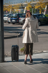 jeune femme de dos avec une valise attendant un taxi sur le parking d'un aéroport