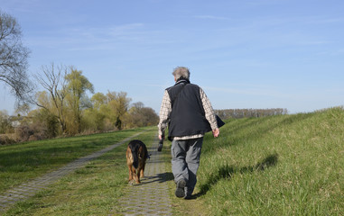 eine frau mit hund an der leine geht an einem deich spazieren