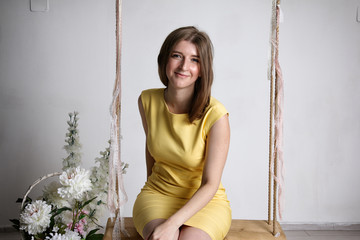 Young girl in yellow dress on swing in white room