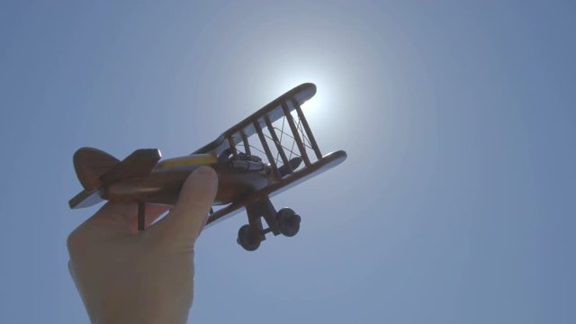 The hand launch a wood plane on the background of a bright sun