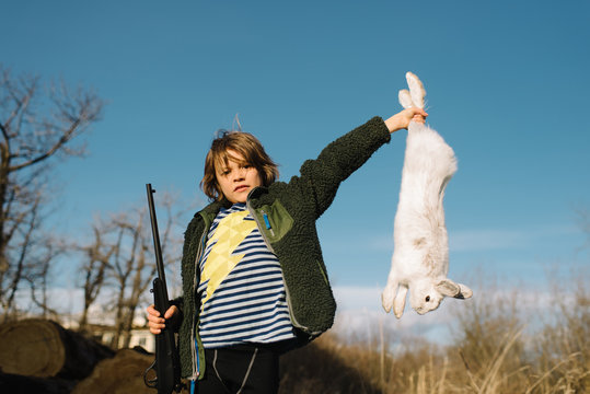 Boy holding up dead rabbit and holding a rifle