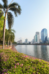 Flowerbed, palm trees and wooden boardwalk at the Benjakiti (Benjakitti) Park and modern skyscrapers in Bangkok, Thailand.