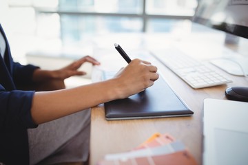 Mid section of graphic designer using graphic tablet at desk