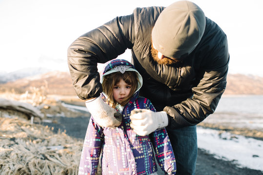 Father putting coat on little girl