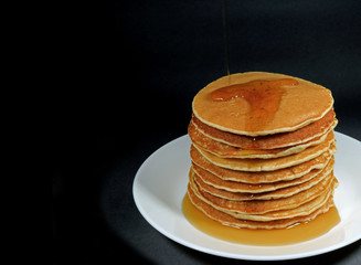 Stack of fresh homemade pancakes with maple syrup served on white plate, black background with free space for text or design 
