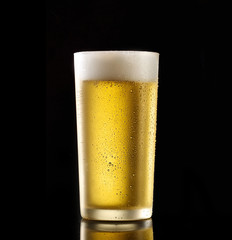 Fresh beer in a glass on a black background. The concept of food.