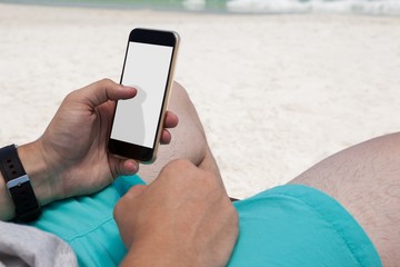 Mid section of man using mobile phone at beach