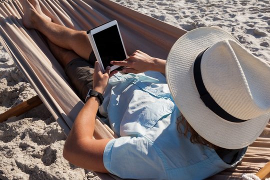 Man relaxing on hammock and using digital tablet on the beach