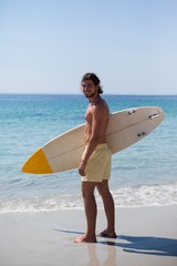 Naklejka na ściany i meble Smiling surfer with surfboard standing at beach coast