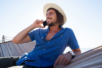 Man relaxing on hammock and talking on mobile phone on the beach