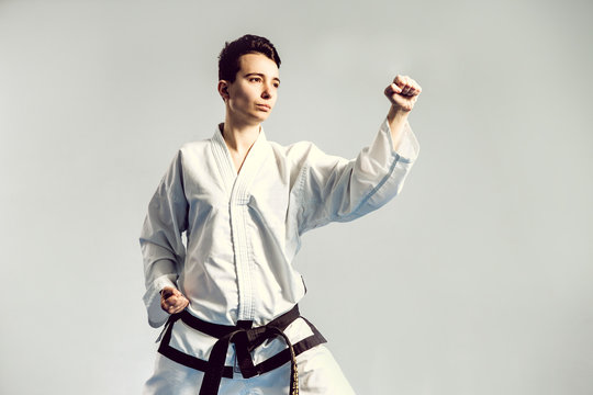 girl in karate suit kimono in studio at grey background. Female child shows judo or karate stans in white uniform with black belt. Individual martial art sport . body portrait