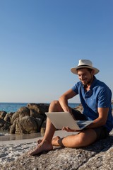 Fototapeta na wymiar Man sitting on the rocks and using laptop on beach