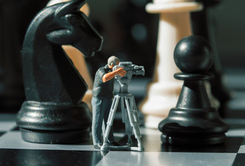 Cameraman miniature doll and chess figures on board. Filming the checkmate game.