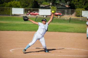 White uniform fast pitch softball pitcher winding up to throw in side view. 