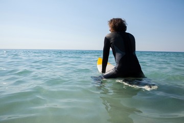 Surfer sitting on surfboard at seacoast