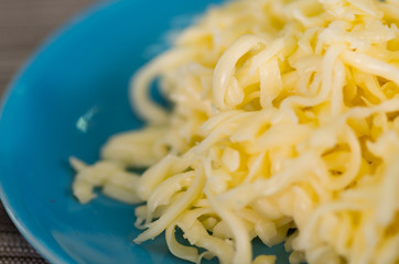 closeup of grated cheese in bowl on wooden background