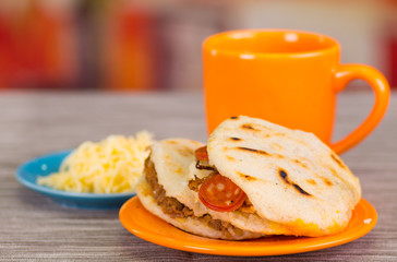 Traditional delicious arepas, shredded chicken avocado and cheddar cheese and shredded beef with a orange cup on wooden blackground