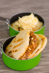 Traditional delicious arepas, shredded chicken avocado and cheddar cheese and shredded beef inside of green saucepan over wooden blackground