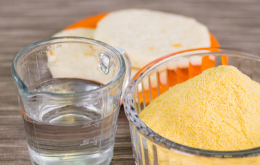 closeup of an arepas flour inside of a cristal bowl, glas of water on wooden blcakground