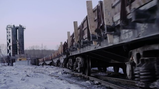 Outlook shot of freight train with empty gondola cars moving along a single-track railway in winter.