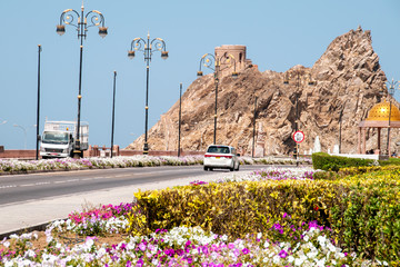 Ulica wzdłuż wybrzeża w Muscat z widokiem na ruiny fortu na skale. - obrazy, fototapety, plakaty