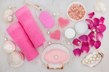 Bathroom and spa beauty treatment accessories with rose petals, himalayan salt, pumice, soaps, pink face towels, shells and pearls on distressed wood background.