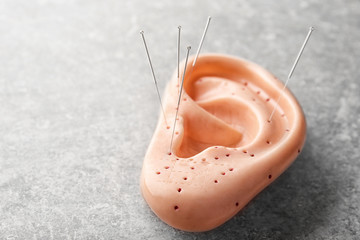 Needles for acupuncture and plastic mockup of human ear on grey background