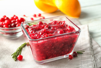 Delicious cranberry sauce in glass bowl on wooden background, close up