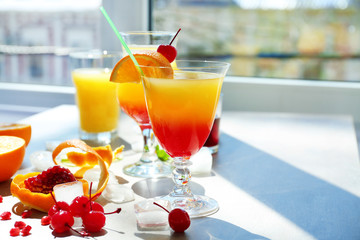 Glasses of Tequila Sunrise cocktail with ingredients on table