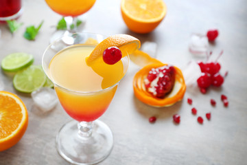 Glass of Tequila Sunrise cocktail with ingredients on grey background
