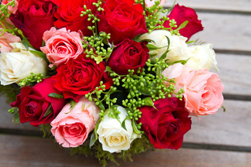  Rosengesteck mit roten, rosafarbenen und weißen Rosen auf einem Holztisch