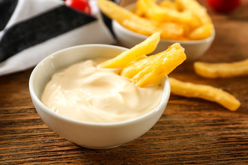 Bowl with tasty mayonnaise sauce and French fries on wooden table, closeup