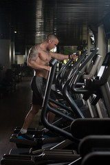 Fototapeta na wymiar Athlete Doing Aerobics Elliptical Walker In Gym