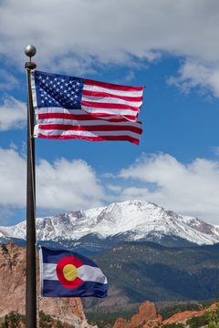 American And Colorado Flag Waving In The Wind With Mountains In The Background