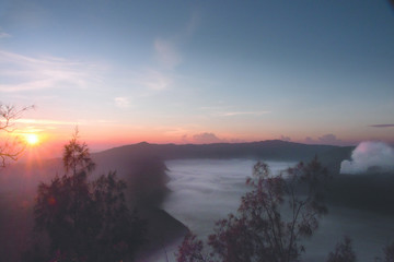 Mist hovering towards the active volcano Bromo in the morning during orange sunrise, at the Tengger Semeru National Park in East Java, Indonesia.